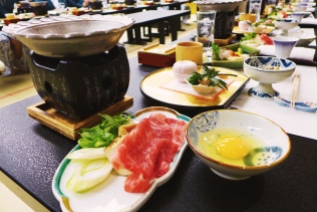 Sukiyaki, prepared and served in a shallow iron hot pot resting on top of its etched stand. Foreground: slices of beef, leeks, and scallions moments before simmering in a mixture of soy sauce, sugar, and miriin. The egg was beaten and used as a dipping sauce for the cooked meat and assorted vegetables.